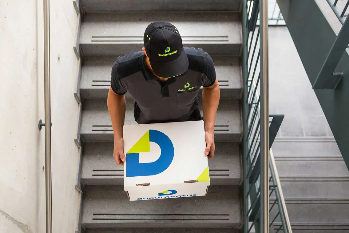 Documentus-Mitarbeiter trägt Archivbox eine Treppe herunter